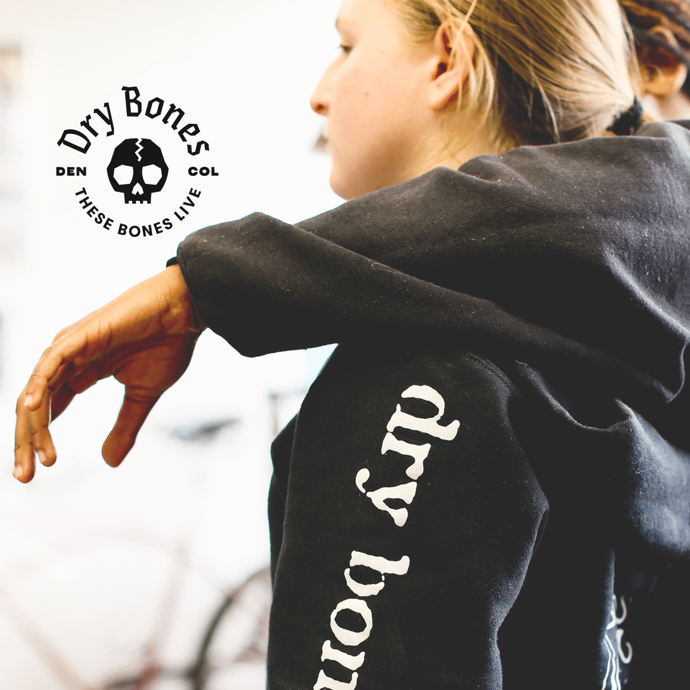 Person wearing a black hoodie with 'Dry Bones' branding, with a blurred background.