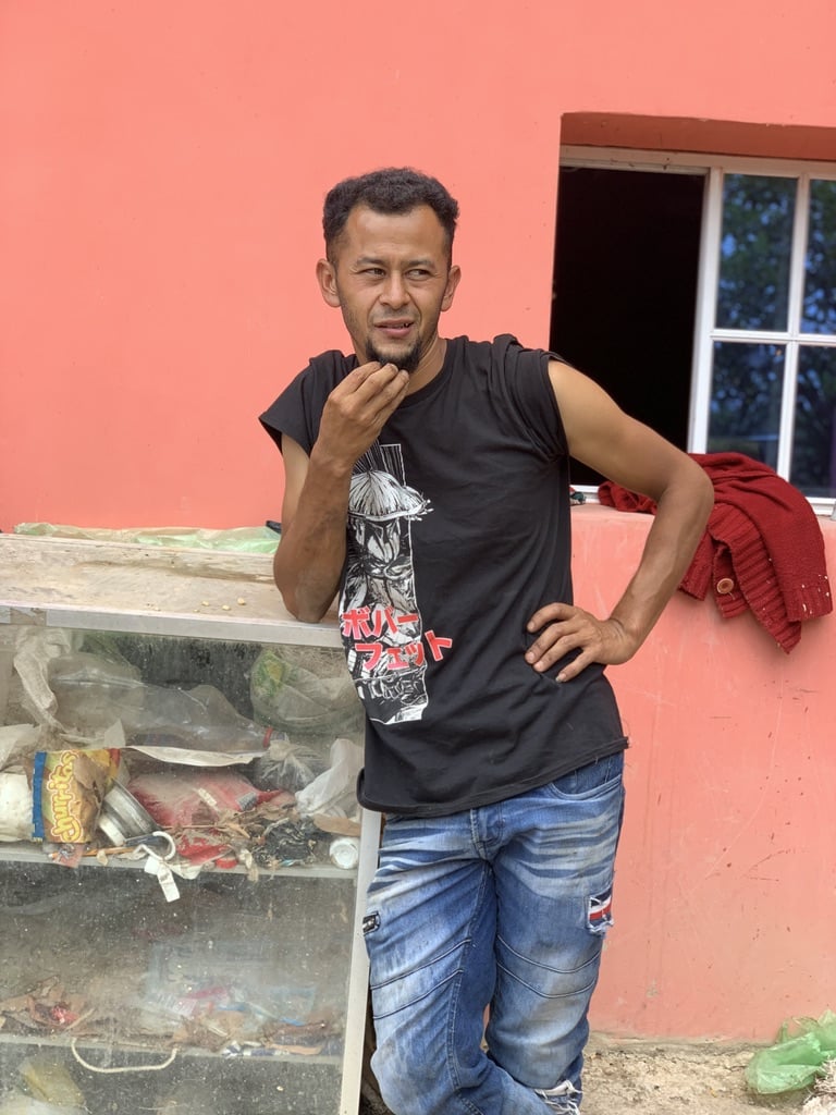 Nelson Flores standing in front of a pink wall with a window, wearing a black sleeveless shirt and blue jeans.