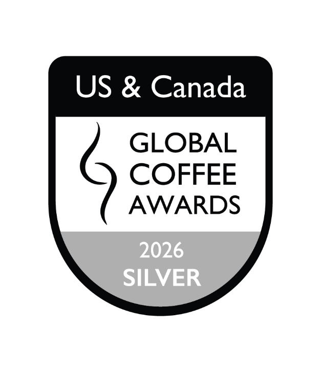 US & Canada Global Coffee Awards 2026 Silver badge emblem, featuring a shield design with black, white, and gray sections and the text 'GLOBAL COFFEE AWARDS 2026 SILVER'.